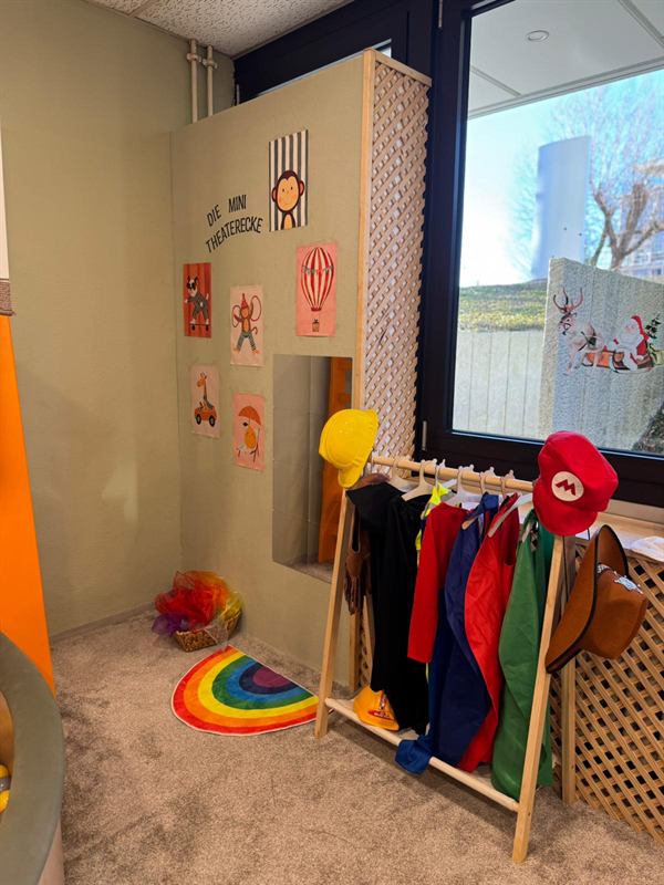 Verkleidungsecke mit Kostümen und Regenbogen-Teppich in der Kinder-Spielecke des Familiencafés Zauberbaum
